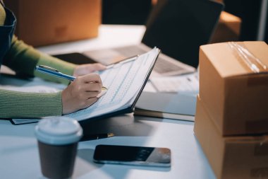 Girişim KOBİ küçük işletme girişimcisi önlük giyen Asyalı kadın dizüstü bilgisayar ve kutu kullanarak çevrimiçi müşterilere, çevrimiçi sme iş fikirlerine satış hazırlamak için siparişleri alır ve gözden geçirir.