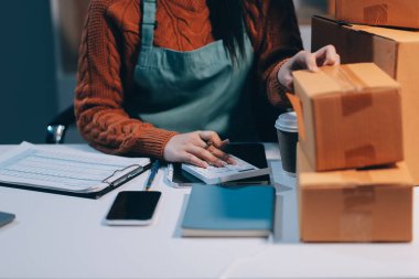 Girişim KOBİ küçük işletme girişimcisi önlük giyen Asyalı kadın dizüstü bilgisayar ve kutu kullanarak çevrimiçi müşterilere, çevrimiçi sme iş fikirlerine satış hazırlamak için siparişleri alır ve gözden geçirir.
