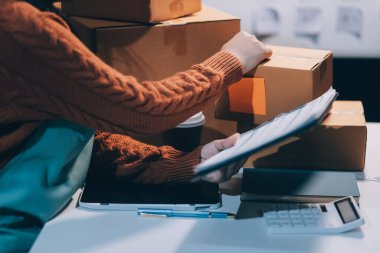 Girişim KOBİ küçük işletme girişimcisi önlük giyen Asyalı kadın dizüstü bilgisayar ve kutu kullanarak çevrimiçi müşterilere, çevrimiçi sme iş fikirlerine satış hazırlamak için siparişleri alır ve gözden geçirir.