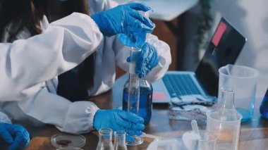 Koruyucu eldivenler ve gözlüklü kadın bilim adamı laboratuarda test tüpü tutuyor.