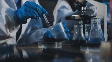 Bir kimya laboratuvarında elinde bir bardak kimyasal sıvı tutan bir bilim adamının yakın plan fotoğrafı..