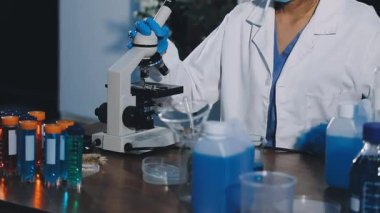 Koruyucu eldivenler giymiş laboratuar bilim adamı elinde şişe tutuyor.