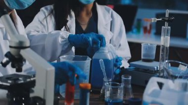 Laboratuvar önlüklü bilim adamı elinde cam tüplerle sıvıya bakıyor.