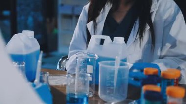 Koruyucu gözlüklü genç bir kadın laboratuarda otururken mikroskoba bakıyor.