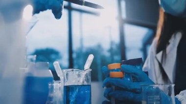 Mavi koruyucu kıyafetli bilim adamı elinde sıvı test tüpü tutuyor.