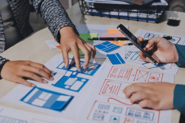 Çalışan bir toplantı sırasında uxui mobil uygulama şablonlarını analiz eden bir grup genç uygulama geliştirici