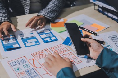 Çalışan bir toplantı sırasında uxui mobil uygulama şablonlarını analiz eden bir grup genç uygulama geliştirici