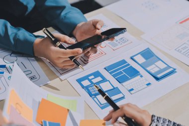 Çalışan bir toplantı sırasında uxui mobil uygulama şablonlarını analiz eden bir grup genç uygulama geliştirici