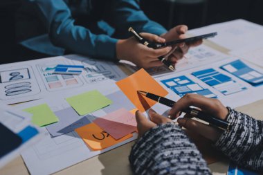 Çalışan bir toplantı sırasında uxui mobil uygulama şablonlarını analiz eden bir grup genç uygulama geliştirici