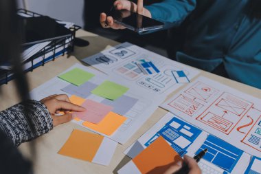 Çalışan bir toplantı sırasında uxui mobil uygulama şablonlarını analiz eden bir grup genç uygulama geliştirici