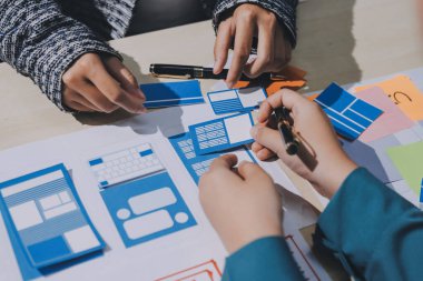 Çalışan bir toplantı sırasında uxui mobil uygulama şablonlarını analiz eden bir grup genç uygulama geliştirici