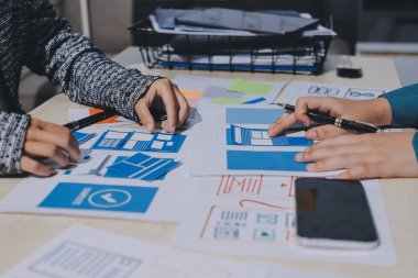 Çalışan bir toplantı sırasında uxui mobil uygulama şablonlarını analiz eden bir grup genç uygulama geliştirici