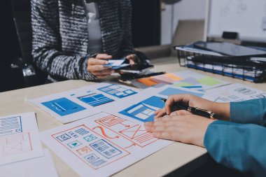 Çalışan bir toplantı sırasında uxui mobil uygulama şablonlarını analiz eden bir grup genç uygulama geliştirici