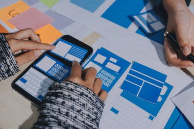 Çalışan bir toplantı sırasında uxui mobil uygulama şablonlarını analiz eden bir grup genç uygulama geliştirici