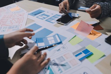 Çalışan bir toplantı sırasında uxui mobil uygulama şablonlarını analiz eden bir grup genç uygulama geliştirici