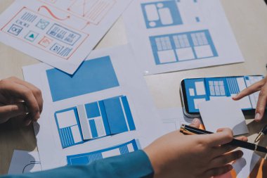 Çalışan bir toplantı sırasında uxui mobil uygulama şablonlarını analiz eden bir grup genç uygulama geliştirici