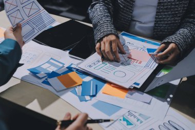 Çalışan bir toplantı sırasında uxui mobil uygulama şablonlarını analiz eden bir grup genç uygulama geliştirici