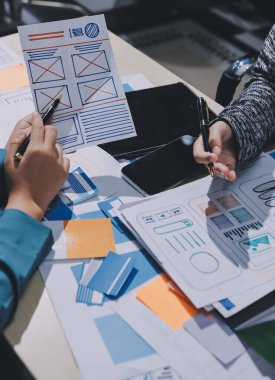 Çalışan bir toplantı sırasında uxui mobil uygulama şablonlarını analiz eden bir grup genç uygulama geliştirici