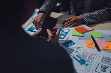 Çalışan bir toplantı sırasında uxui mobil uygulama şablonlarını analiz eden bir grup genç uygulama geliştirici