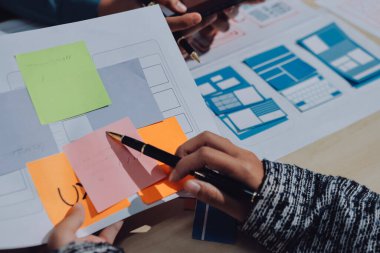 Çalışan bir toplantı sırasında uxui mobil uygulama şablonlarını analiz eden bir grup genç uygulama geliştirici