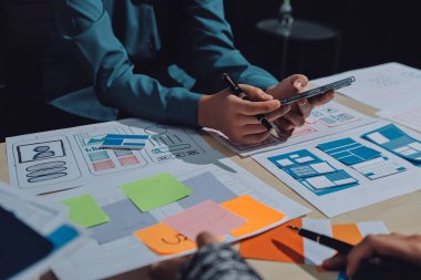 Çalışan bir toplantı sırasında uxui mobil uygulama şablonlarını analiz eden bir grup genç uygulama geliştirici