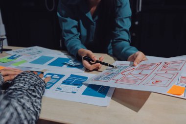 Çalışan bir toplantı sırasında uxui mobil uygulama şablonlarını analiz eden bir grup genç uygulama geliştirici