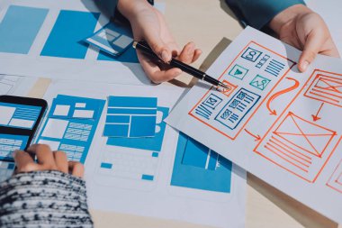 Çalışan bir toplantı sırasında uxui mobil uygulama şablonlarını analiz eden bir grup genç uygulama geliştirici