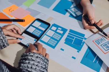 Çalışan bir toplantı sırasında uxui mobil uygulama şablonlarını analiz eden bir grup genç uygulama geliştirici