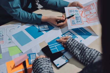 Çalışan bir toplantı sırasında uxui mobil uygulama şablonlarını analiz eden bir grup genç uygulama geliştirici