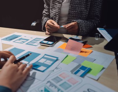 Çalışan bir toplantı sırasında uxui mobil uygulama şablonlarını analiz eden bir grup genç uygulama geliştirici