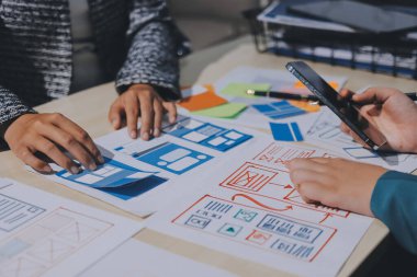 Çalışan bir toplantı sırasında uxui mobil uygulama şablonlarını analiz eden bir grup genç uygulama geliştirici