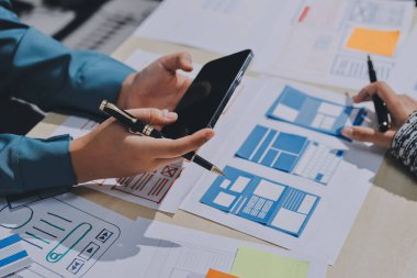 Çalışan bir toplantı sırasında uxui mobil uygulama şablonlarını analiz eden bir grup genç uygulama geliştirici