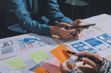 Çalışan bir toplantı sırasında uxui mobil uygulama şablonlarını analiz eden bir grup genç uygulama geliştirici