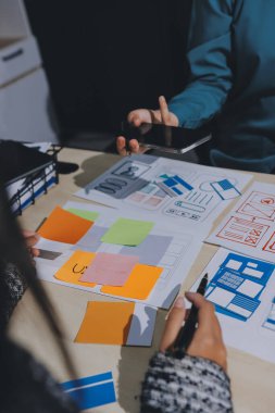 Çalışan bir toplantı sırasında uxui mobil uygulama şablonlarını analiz eden bir grup genç uygulama geliştirici