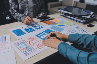 Çalışan bir toplantı sırasında uxui mobil uygulama şablonlarını analiz eden bir grup genç uygulama geliştirici