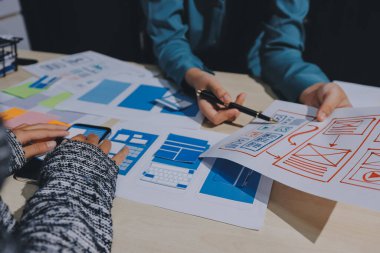 Çalışan bir toplantı sırasında uxui mobil uygulama şablonlarını analiz eden bir grup genç uygulama geliştirici