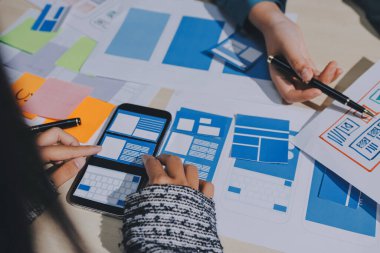 Çalışan bir toplantı sırasında uxui mobil uygulama şablonlarını analiz eden bir grup genç uygulama geliştirici