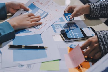 Çalışan bir toplantı sırasında uxui mobil uygulama şablonlarını analiz eden bir grup genç uygulama geliştirici