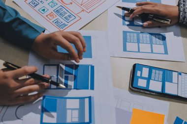 Çalışan bir toplantı sırasında uxui mobil uygulama şablonlarını analiz eden bir grup genç uygulama geliştirici