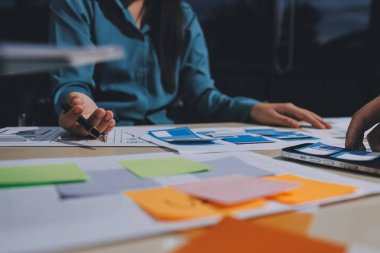 Çalışan bir toplantı sırasında uxui mobil uygulama şablonlarını analiz eden bir grup genç uygulama geliştirici