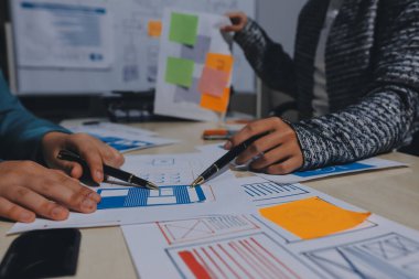 Çalışan bir toplantı sırasında uxui mobil uygulama şablonlarını analiz eden bir grup genç uygulama geliştirici