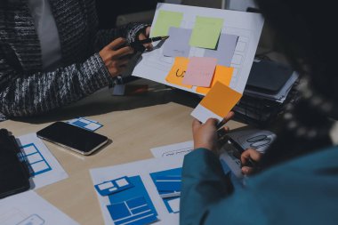 Çalışan bir toplantı sırasında uxui mobil uygulama şablonlarını analiz eden bir grup genç uygulama geliştirici