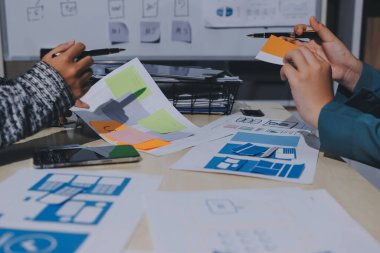 Çalışan bir toplantı sırasında uxui mobil uygulama şablonlarını analiz eden bir grup genç uygulama geliştirici