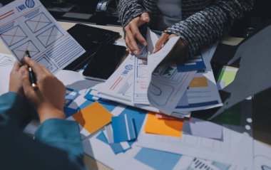 Çalışan bir toplantı sırasında uxui mobil uygulama şablonlarını analiz eden bir grup genç uygulama geliştirici