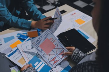 Çalışan bir toplantı sırasında uxui mobil uygulama şablonlarını analiz eden bir grup genç uygulama geliştirici