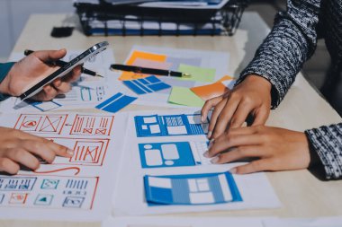 Çalışan bir toplantı sırasında uxui mobil uygulama şablonlarını analiz eden bir grup genç uygulama geliştirici