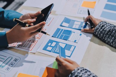 Çalışan bir toplantı sırasında uxui mobil uygulama şablonlarını analiz eden bir grup genç uygulama geliştirici