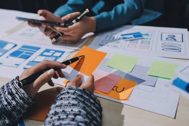 Çalışan bir toplantı sırasında uxui mobil uygulama şablonlarını analiz eden bir grup genç uygulama geliştirici