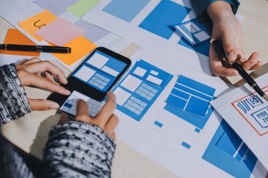 Çalışan bir toplantı sırasında uxui mobil uygulama şablonlarını analiz eden bir grup genç uygulama geliştirici