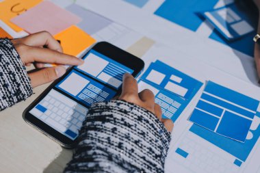 Çalışan bir toplantı sırasında uxui mobil uygulama şablonlarını analiz eden bir grup genç uygulama geliştirici